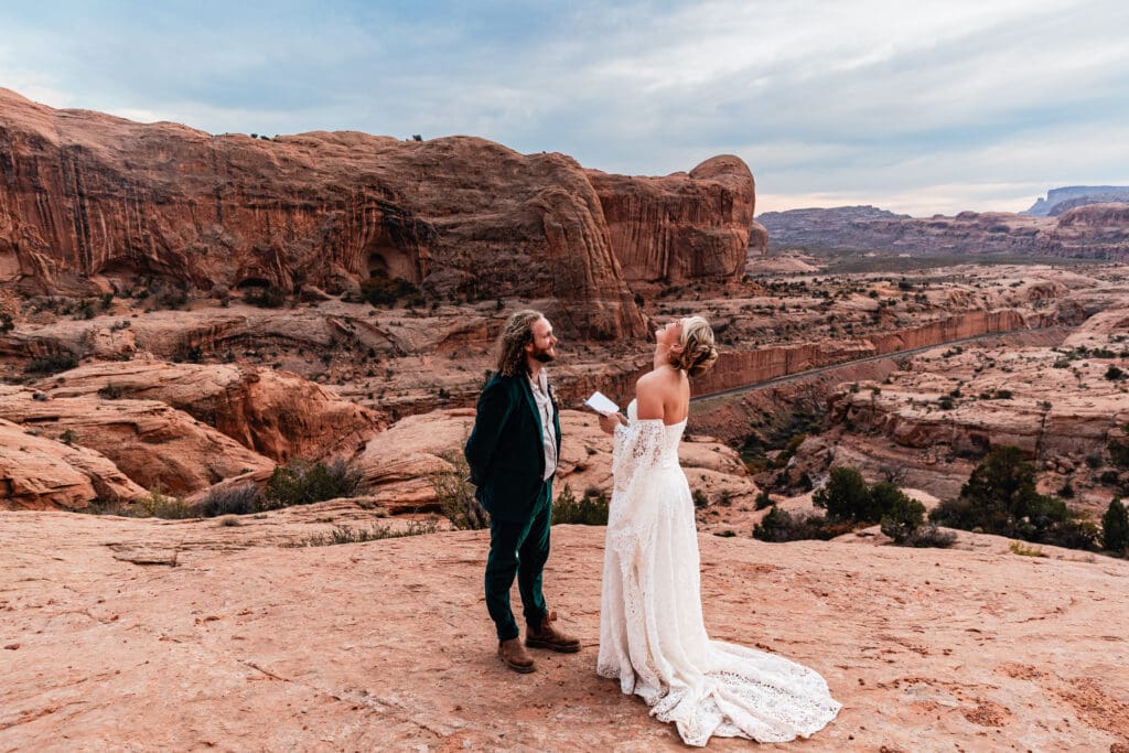 Eloping couple laughing together during their ceremony while exchanging vows beneath Corona Arch in the Moab desert.