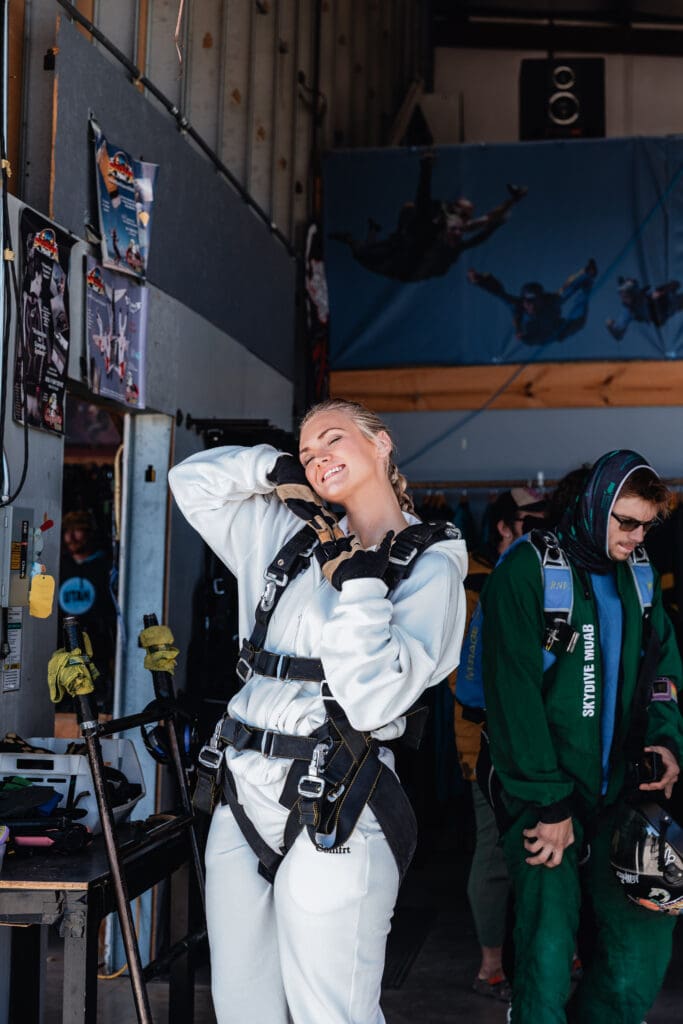 Bride poses after having her skydiving harness adjusted before a tandem jump as part of the couple’s adventure elopement experience.