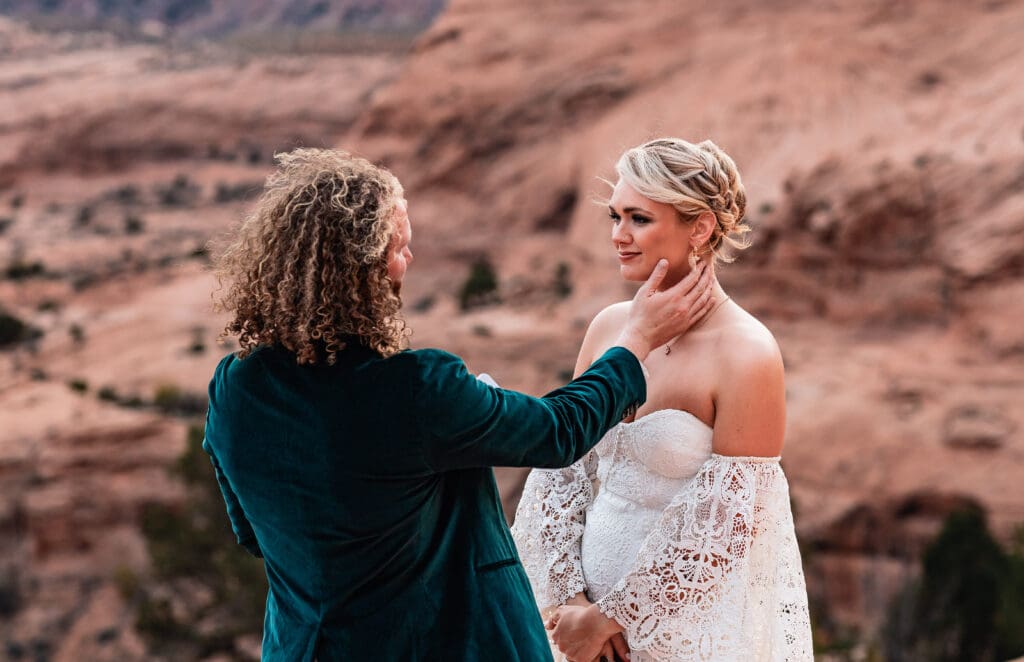 Groom gently caressing the bride’s face during their emotional elopement ceremony at Corona Arch outside Moab, Utah.