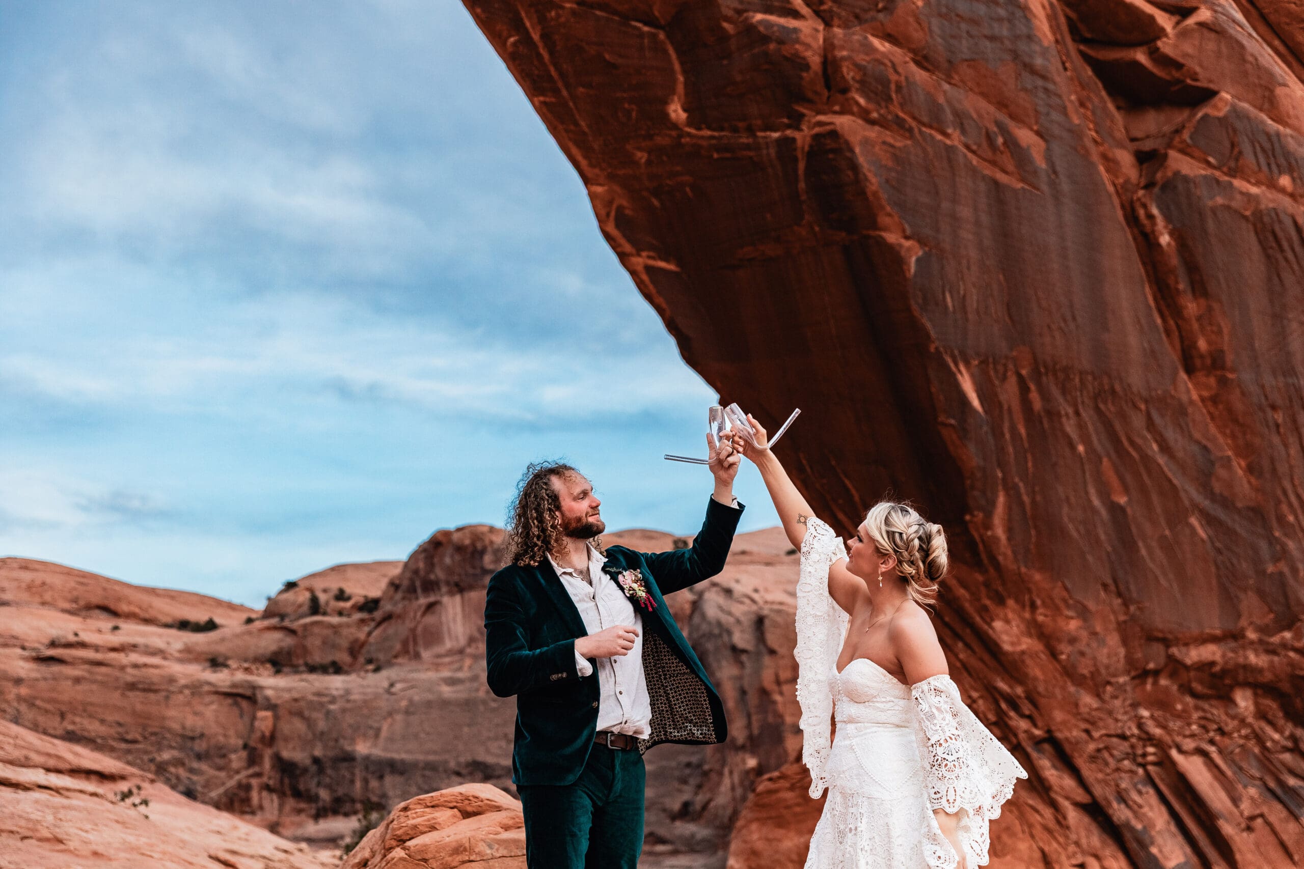 Just-married couple cheering and drinking champagne from champbongs after their elopement ceremony at Corona Arch near Moab, Utah.
