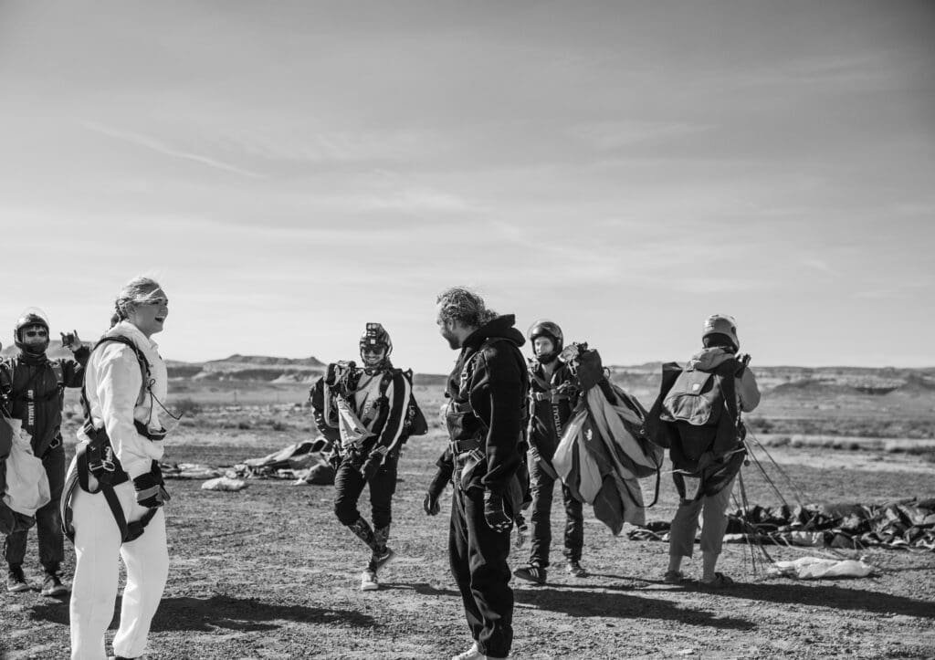 Just-landed couple celebrating and hugging on the ground after completing their tandem skydive on their adventurous elopement day.