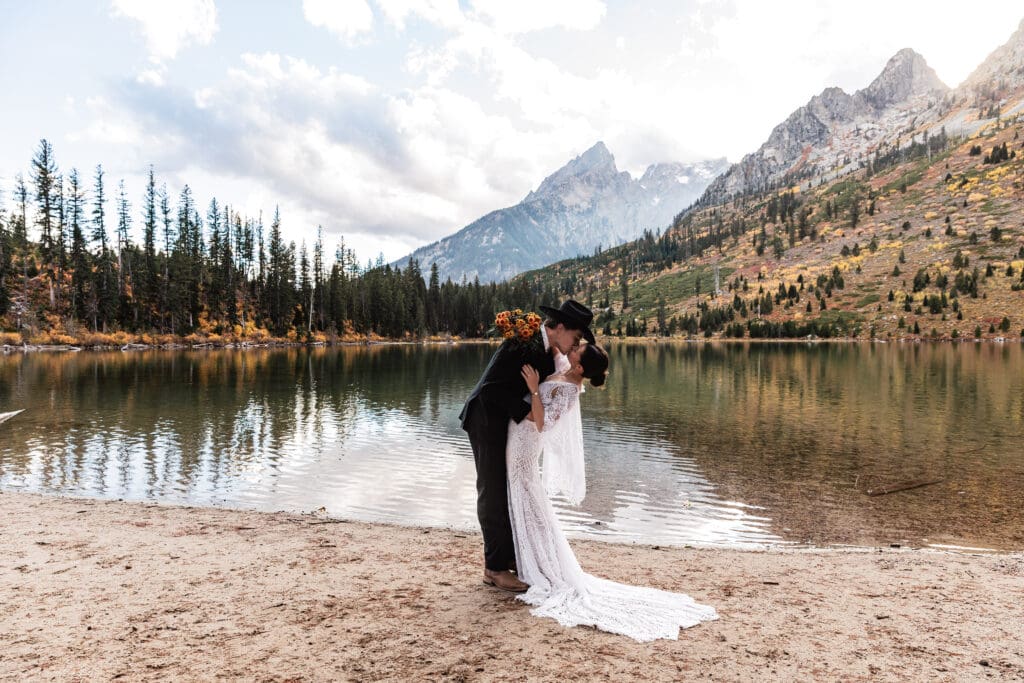 Groom dipping the bride into a kiss along the shoreline of String Lake with the Teton mountains towering in the distance.