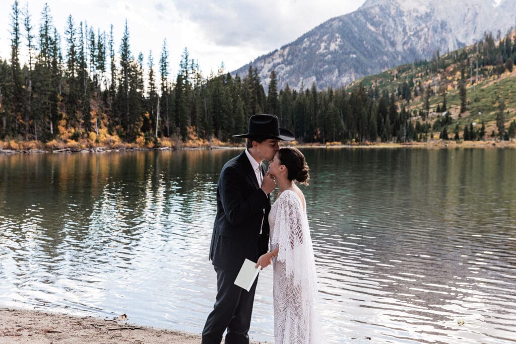 Eloping couple sharing personal vows beside the calm water of String Lake with the Tetons behind them.