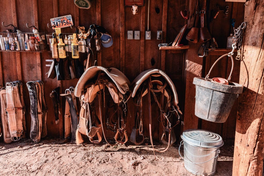 Close-up detail of a leather saddle and riding gear inside a rustic barn during the horseback portion of an adventure elopement.