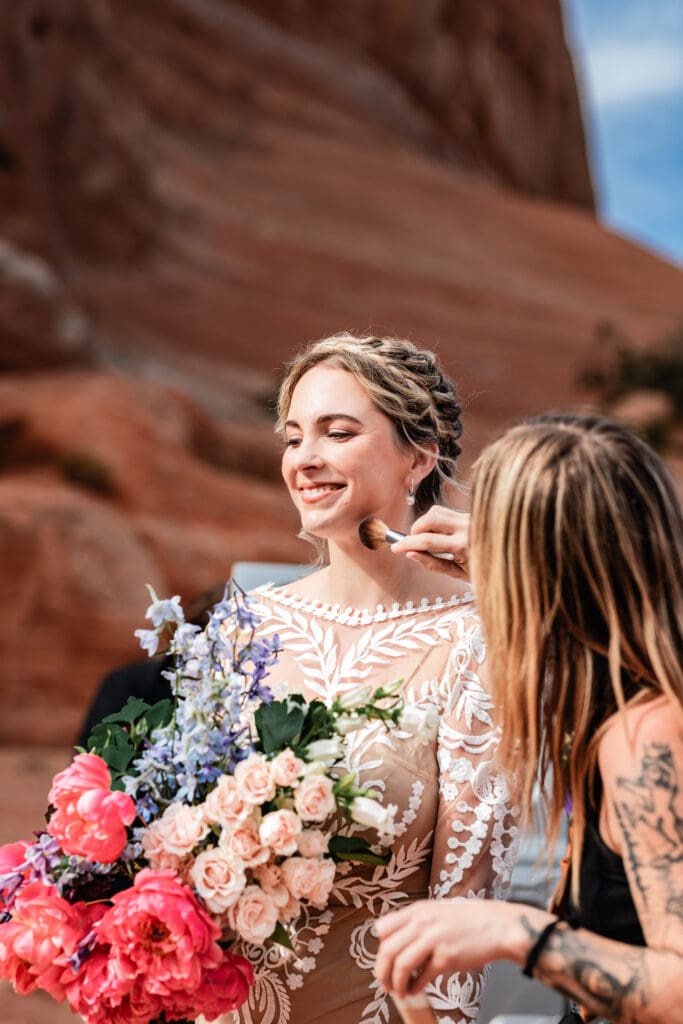 Hair stylist and makeup artist fixing the bride’s hair while preparing for an outdoor adventure elopement in Moab.