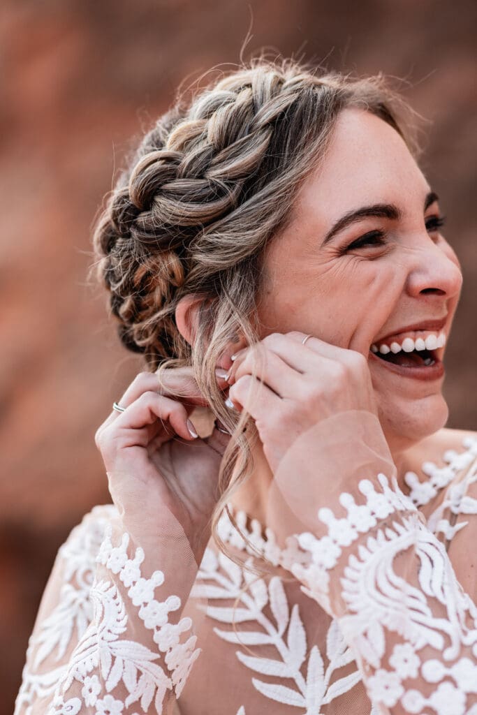 Close-up of the bride laughing while adjusting her hair and jewelry during a candid getting ready moment for her Moab elopement.