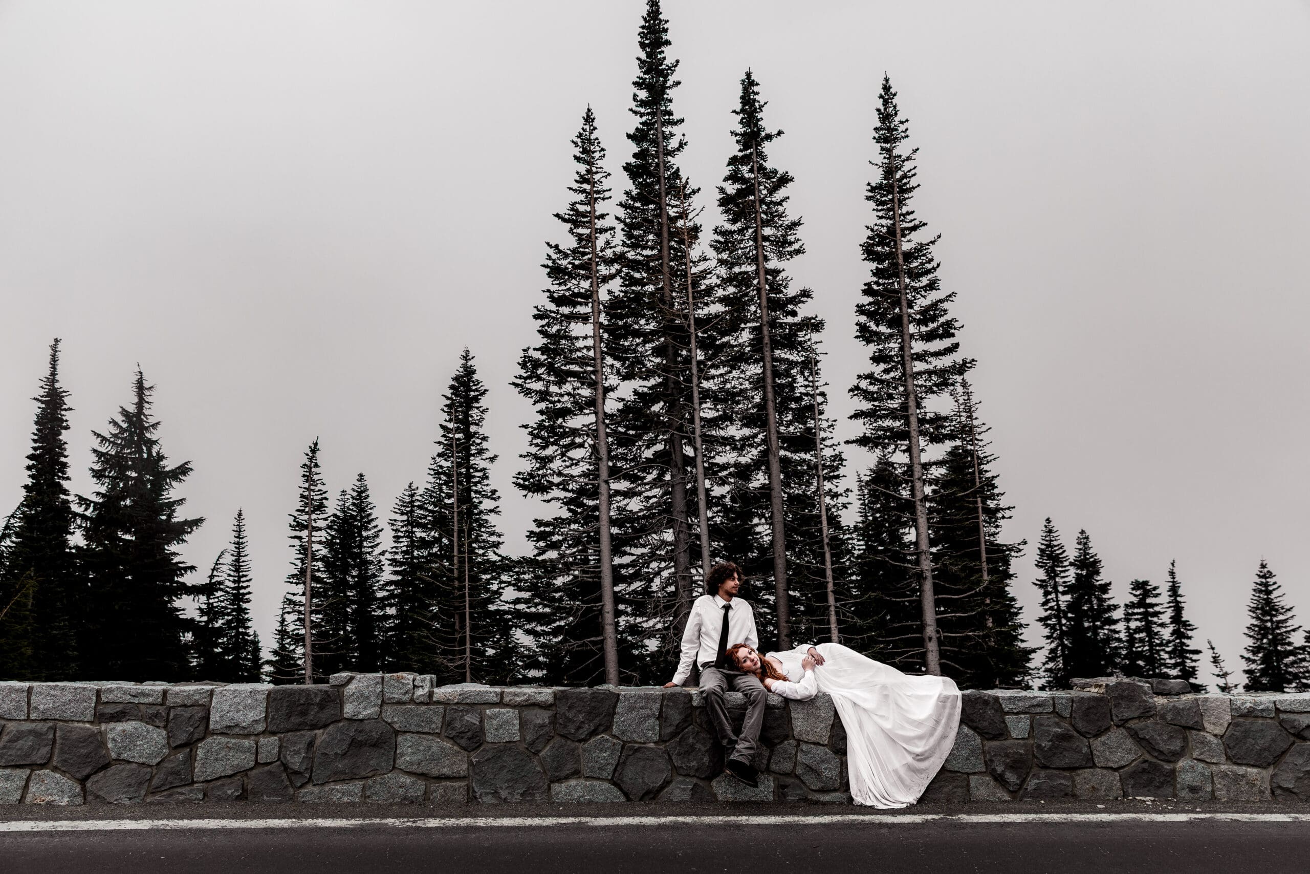 Eloping couple sitting together on a stone wall surrounded by forest in Mount Rainier National Park.