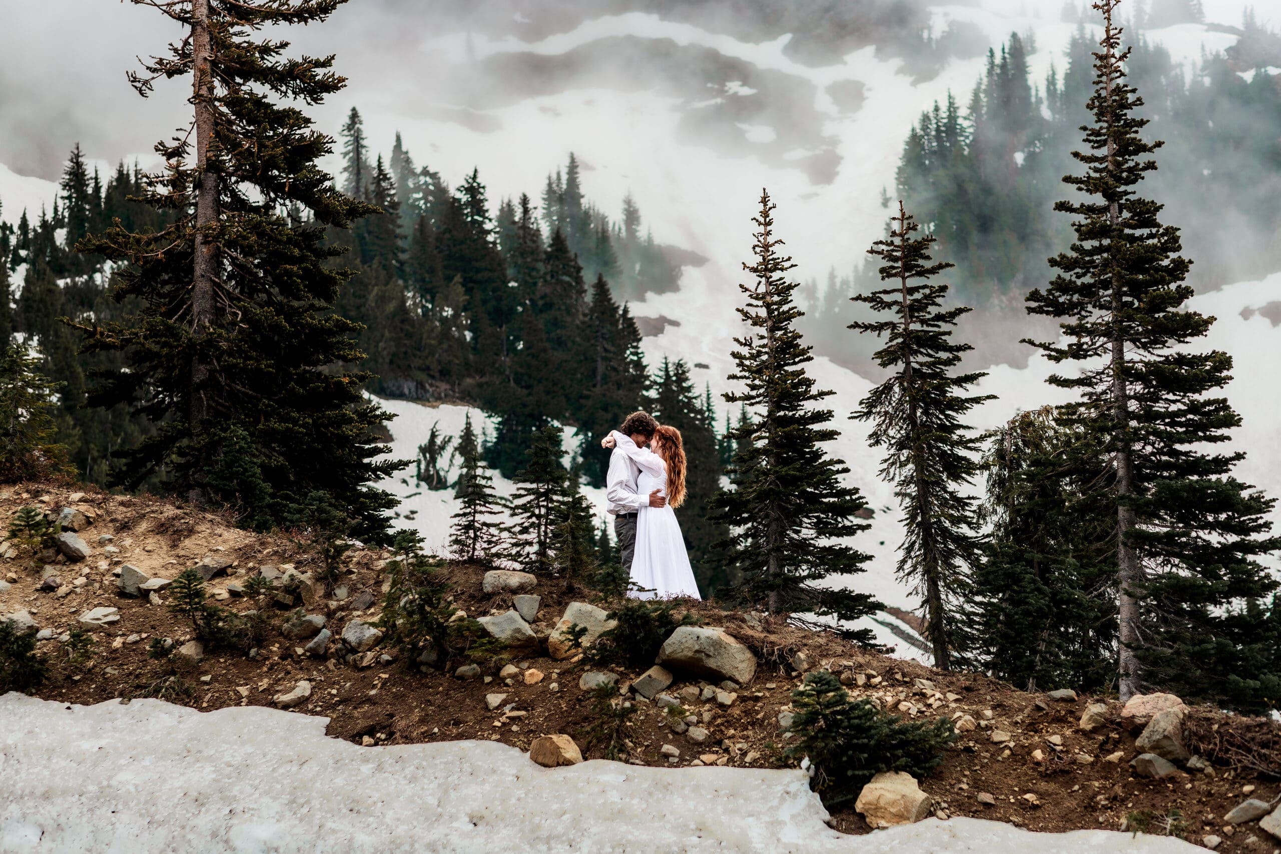 Couple embracing beside the shoreline of Tipsoo Lake with Mount Rainier towering in the distance.