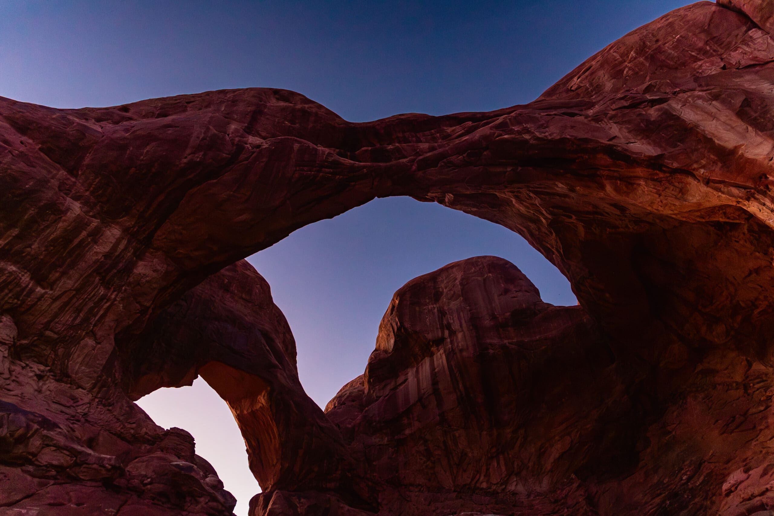 Double Arch in Arches National Park at dusk with warm desert tones, soft fading light, and massive natural sandstone arches set against the Moab Utah sky