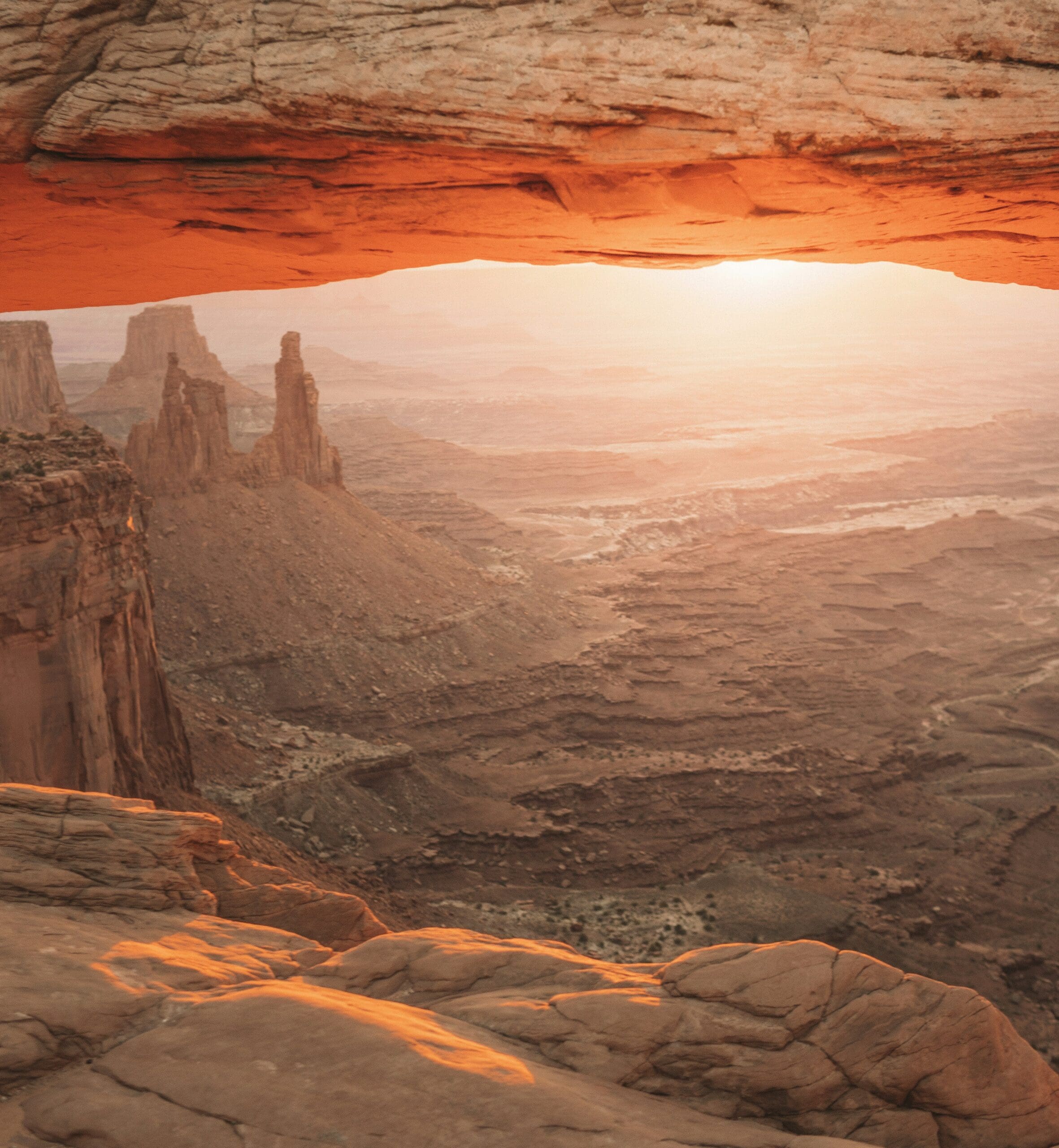 Sunrise light glowing through Mesa Arch in Canyonlands National Park with warm orange sky and canyon view framed by the arch.