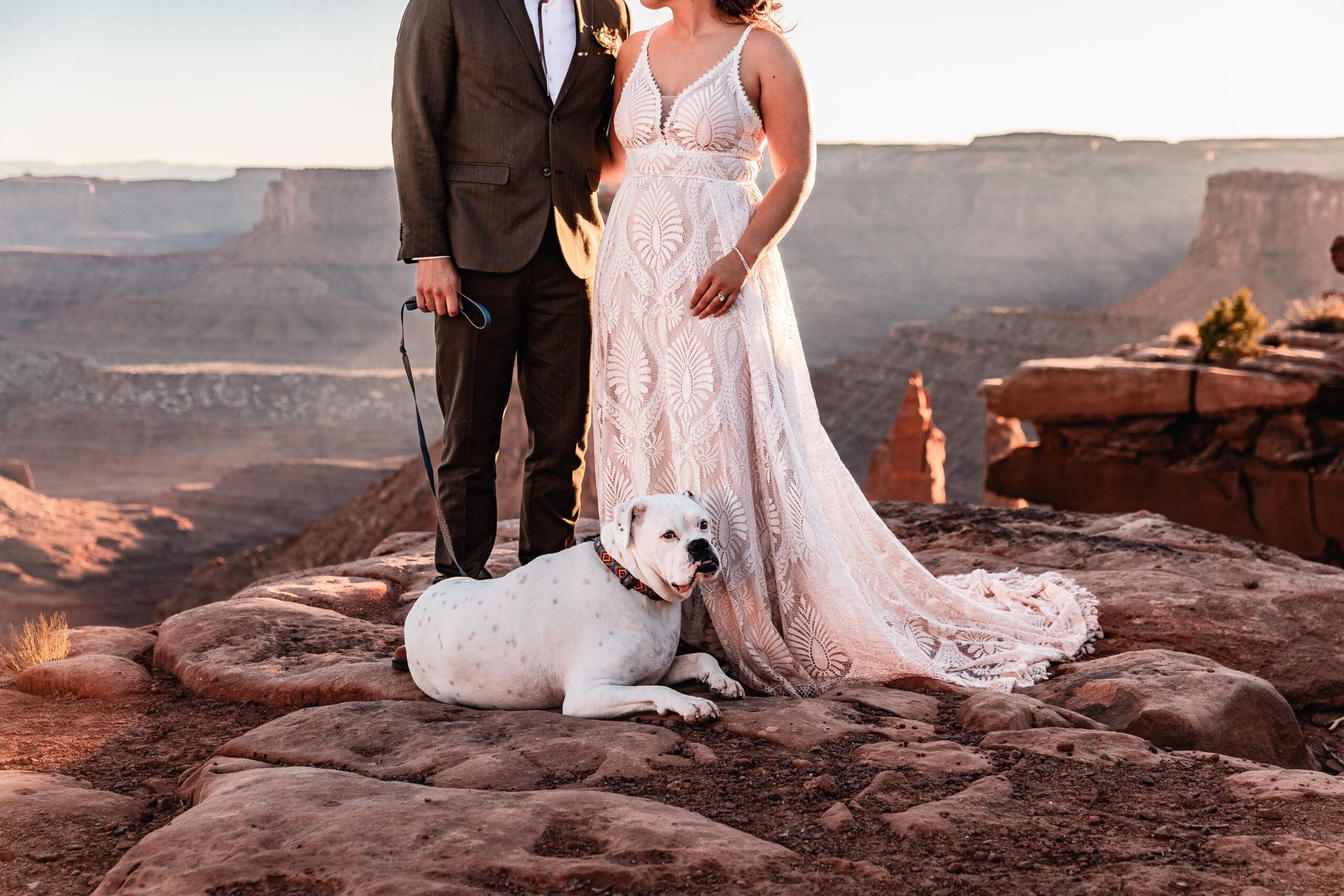 Close-up of a dog sitting at a couple’s feet during their Moab elopement with desert textures and warm tones in the background