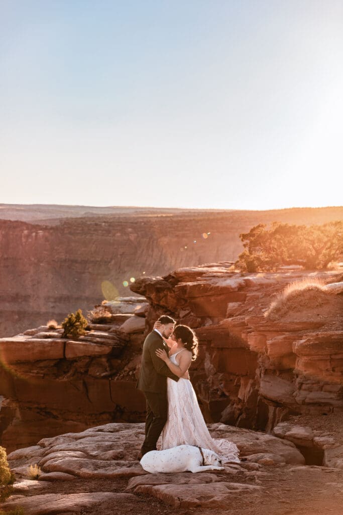 Couple sharing a kiss after their Moab elopement ceremony with their dog standing at their feet surrounded by red rock scenery