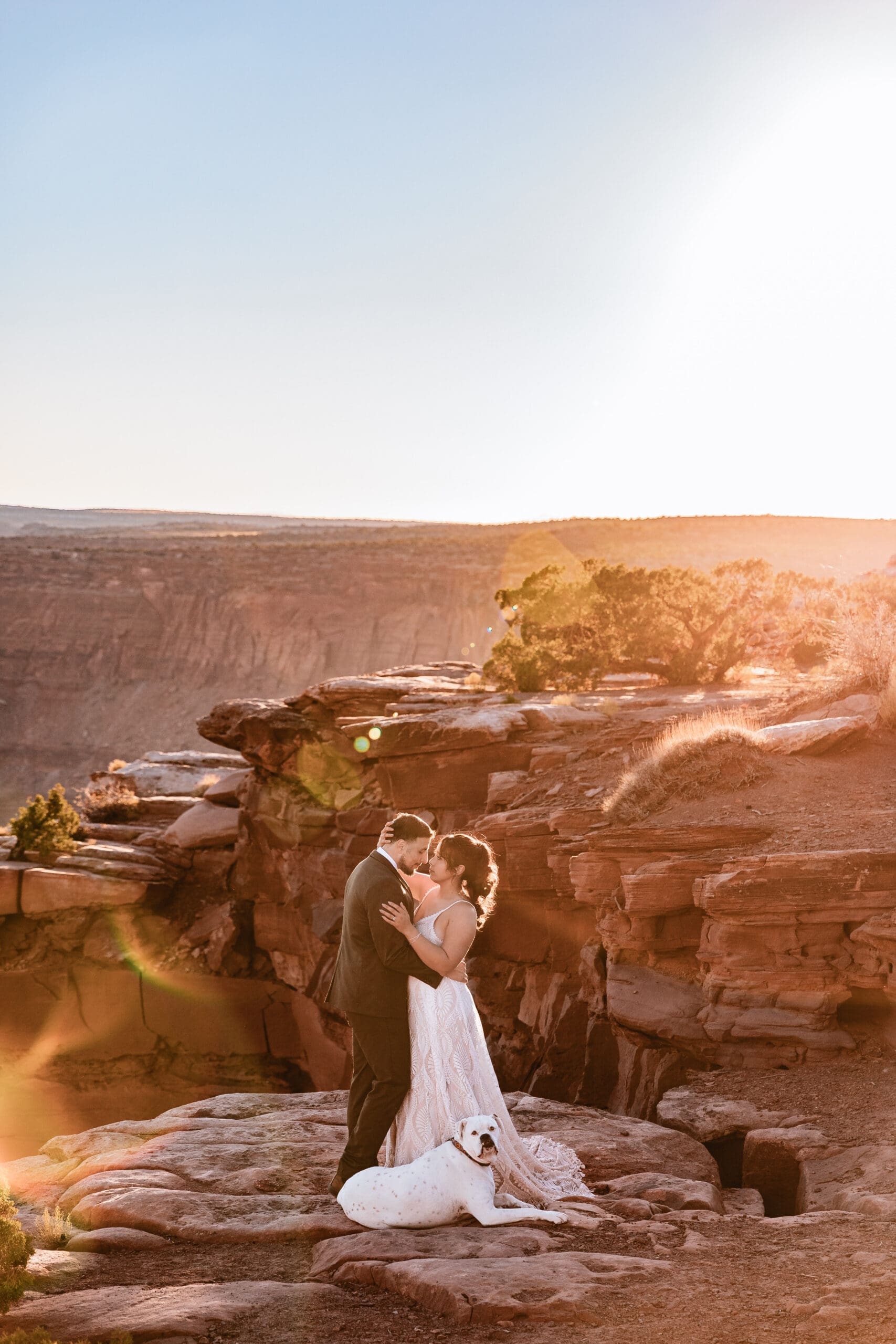 Couple hugging after their elopement ceremony in Moab with their dog sitting at their feet in the desert landscape